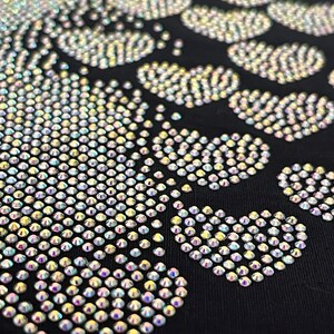 May include: A black fabric background with a design of iridescent rhinestones in the shape of a footprint.