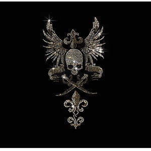 Op de afbeelding: Een sprankelend gouden strassontwerp op een zwarte achtergrond. Het ontwerp toont een schedel met vleugels, gekruiste zwaarden en een fleur-de-lis. Het ontwerp is gemaakt van vele kleine, glinsterende strasssteentjes.