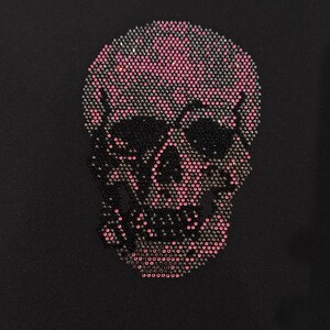 May include: A black skull design, embellished with pink and black rhinestones, is centered on a black background. The skull's cranium is pink, while the eye sockets, nose, and jaw are black, creating a striking contrast.