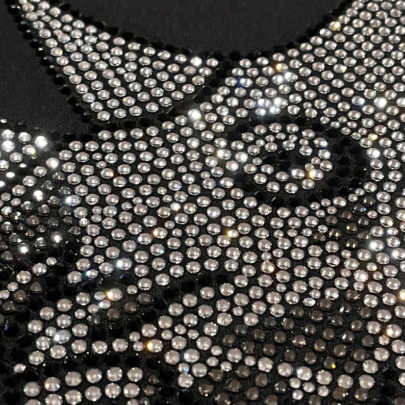 Op de afbeelding: Zwarte stof bedekt met een patroon van zilveren strass steentjes. De strass steentjes zijn gerangschikt in een geometrisch ontwerp.