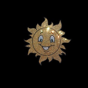 May include: A yellow smiling sun with a face made of rhinestones. The sun has a large smile and two eyes. The sun is surrounded by rays that are also made of rhinestones.