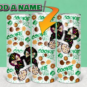 May include: Three white stainless steel tumblers with a green, brown, and white pattern. The pattern features a girl with a bow in her hair, cookies, and the words "Cookie Love!"
