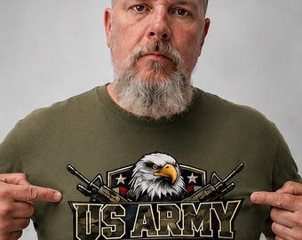 May include: An olive green t-shirt featuring a graphic print of a bald eagle head centered above the text US ARMY in bold letters. The design includes two crossed rifles, a pair of silver dog tags, and a shield background with stars and stripes.