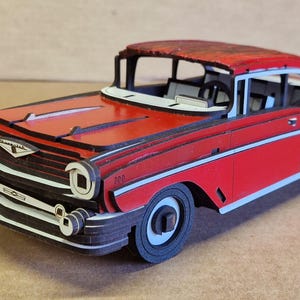 May include: A red and white classic car model with black trim. The model features a detailed design, including headlights, a grill, and a roof. The car is a vintage style, likely from the mid-20th century.