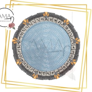 Pode incluir: Um desenho de bordado circular com um Stargate cinza e dourado com um centro azul e um anel de símbolos ao redor da borda.