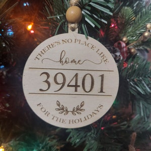 May include: A round wooden Christmas ornament with the text "There's no place like home 39401 for the holidays" engraved on it.