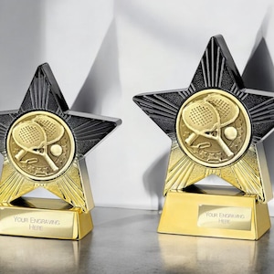 Könnte beinhalten: Zwei goldene und schwarze sternförmige Pokale mit einem Paddleball-Design. Die Basis jedes Pokals trägt den Text "Your Engraving Here".