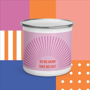 以下が含まれることがあります： ピンク色のバンドに「DO NO HARM TAKE NO SHIT」の文字とサンバーストのデザインが施された白いエナメルマグ。マグカップは銀色の縁があり、カラフルな幾何学模様の背景に配置されています。