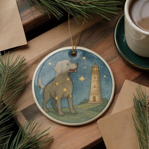 May include: Round ceramic ornament featuring a dog with a constellation design, a lighthouse, and stars against a blue night sky. The ornament has a gold string for hanging. A charming holiday decoration.