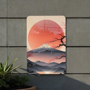 May include: A digital illustration of Mount Fuji with a large red sun behind it. The mountain is surrounded by a blue lake and a forest of trees. The sun is partially obscured by a branch of a cherry blossom tree with pink flowers.