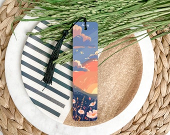 May include: A colorful bookmark with a sunset scene, flowers, and the word "Sunny" at the top. The bookmark has a black tassel.