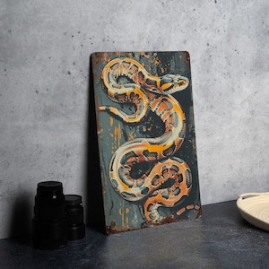 May include: A metal sign with a rusty, distressed look featuring a detailed illustration of a yellow and brown snake coiled on a dark blue background.