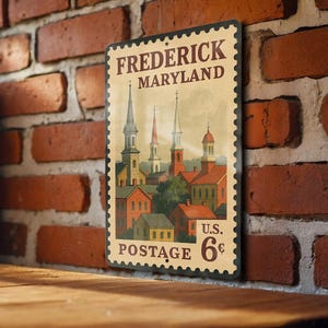 May include: A vintage-style metal sign featuring a detailed illustration of Frederick, Maryland, resembling a postage stamp. The sign showcases buildings with spired rooftops in shades of red, yellow, and green, with the text "Frederick Maryland" and "Postage 6¢".
