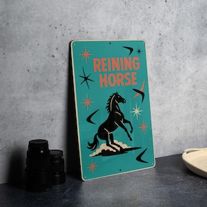 May include: A teal metal sign with the words "REINING HORSE" in orange, and a black horse rearing up. The sign has retro star and boomerang designs.