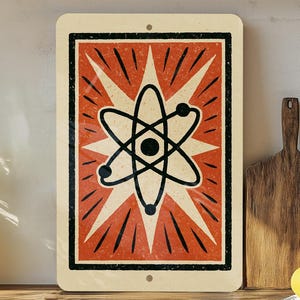 May include: Rectangular metal sign featuring a retro atomic symbol design. The sign has a cream-colored background with a red and black graphic of an atom. The design is reminiscent of vintage science illustrations.