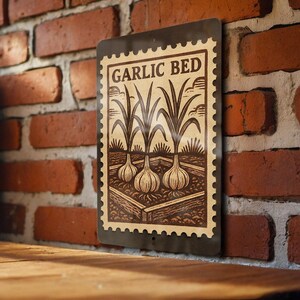 May include: A rectangular metal sign with the words "GARLIC BED" at the top. The sign features a vintage illustration of garlic plants with bulbs and leaves. The sign is mounted on a red brick wall.