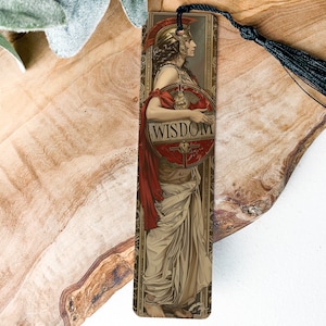 May include: A bookmark featuring a vintage illustration of a woman in a flowing gown holding a shield with the word "WISDOM" on it. The bookmark has a gold background and a black tassel.