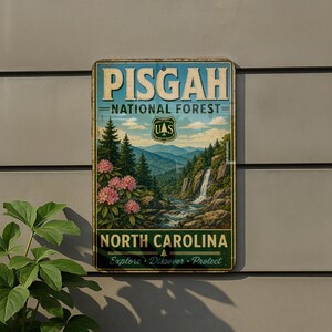 A vintage-style metal sign for Pisgah National Forest in North Carolina, featuring a scenic landscape with pine trees, a waterfall, and pink flowers.