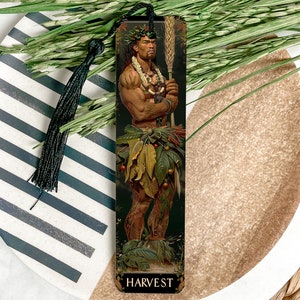 May include: A decorative bookmark featuring a muscular figure adorned with leaves and a crown, holding a staff of wheat. The word "HARVEST" is at the bottom. The bookmark has a black tassel and is set on a decorative plate.