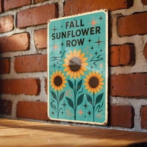 May include: A rectangular metal sign with the text "FALL SUNFLOWER ROW" in teal, featuring three sunflowers. The sign has a distressed, vintage look, with orange starburst and star accents. The background is a brick wall.