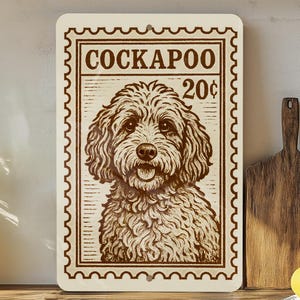 May include: A rectangular sign with a vintage postage stamp design featuring a Cockapoo dog. The sign is cream-colored with brown text and a detailed illustration of the dog. The text reads "COCKAPOO 20¢".