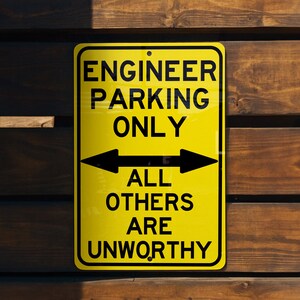 May include: Yellow sign with black text that reads "Engineer Parking Only" with two black arrows pointing in opposite directions. Below the arrows, the sign reads "All Others Are Unworthy".