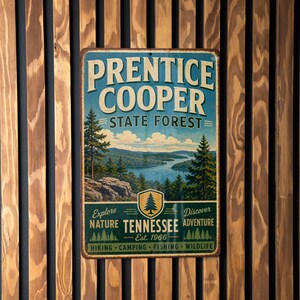 May include: A rectangular metal sign with the text "PRENTICE COOPER STATE FOREST" in white and blue. The sign features a landscape painting of a lake and trees. The sign also includes the text "TENNESSEE Est. 1966" and the words "Explore Nature Discover Adventure".