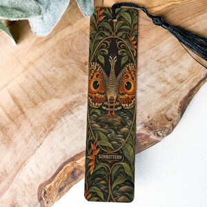 May include: A rectangular bookmark featuring a detailed illustration of a sunbittern bird with orange and brown patterned wings, standing in a stream surrounded by green foliage. The word SUNBITTERN is printed at the bottom, and a black tassel is attached.