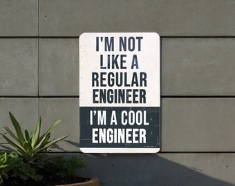 May include: A white sign with black text that reads "I'm not like a regular engineer. I'm a cool engineer." The sign is mounted on a gray wall.
