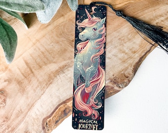 May include: A black bookmark with a silver unicorn with a pink mane and tail. The unicorn is standing on its hind legs with its front legs raised. The background is a dark blue with stars. The text "Magical Journey" is printed at the bottom of the bookmark.
