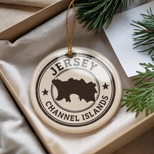 A Jersey Channel Islands ornament is displayed in a box, surrounded by pine branches.