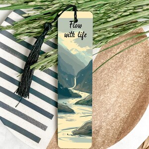 May include: A bookmark with a mountain river scene and the text "Flow with life". The bookmark is cream colored with a black tassel.