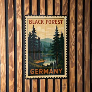 May include: A rectangular metal sign featuring a vintage travel poster design of the Black Forest in Germany. The artwork depicts a forest scene with a lake and mountains, framed by a postage stamp border. The sign is mounted on a wooden slat wall.