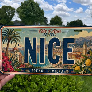 May include: A rectangular metal sign featuring the word NICE in large dark blue letters. The background displays a scenic illustration of the French Riviera, including a palm tree, a coastal city, mountains, and yellow lemons on a branch.
