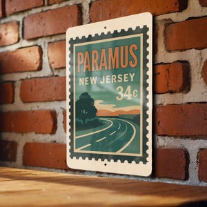May include: A rectangular metal sign with a vintage design. The sign features the word "PARAMUS" in orange, "NEW JERSEY" in white, and "34c" in green. The design includes a road, tree, and sunset.