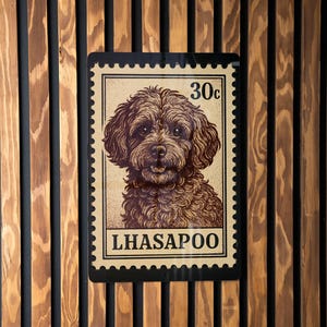 May include: A rectangular sign resembling a postage stamp, featuring a brown illustration of a dog's face. The stamp reads "30c" and "LHASAPOO" in a serif font. The sign is mounted on a wooden wall with vertical slats.