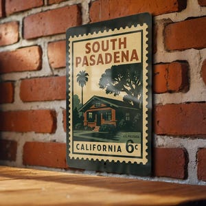 May include: A vintage-style metal sign featuring a stylized illustration of a house and palm tree, with the text "SOUTH PASADENA CALIFORNIA 6¢". The sign has a black border and is mounted on a brick wall.