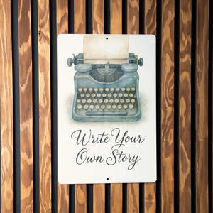 May include: A white metal sign with a watercolor illustration of a vintage typewriter and the text "Write Your Own Story".