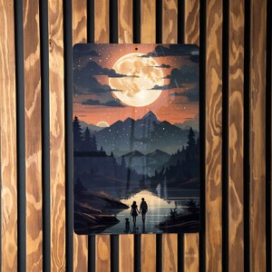 May include: Metal wall art featuring a serene landscape with a large, glowing moon in a twilight sky. The artwork depicts a couple and a dog walking along a lake, with mountains and trees in the background. The art is displayed on a wooden wall.