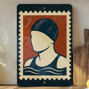 May include: Rectangular metal sign featuring a vintage-style illustration of a swimmer in a cap and swimsuit, set against a red background. The sign has a dark blue border with a postage stamp design. The image is mounted on a wooden surface.