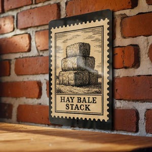 May include: A rectangular metal sign with a vintage design. The sign features a stack of hay bales in a sepia tone, with the words "HAY BALE STACK" in a bold font. The sign has a black border and is mounted on a brick wall.