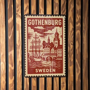 May include: A rectangular sign with a vintage design featuring the word "GOTHENBURG" at the top and "SWEDEN" at the bottom. The sign depicts a ship, buildings, and a bridge in red and cream colors. The sign is mounted on a wooden wall.