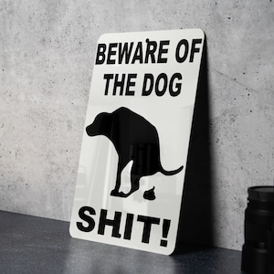 May include: White metal sign with black text and a silhouette of a dog pooping. The sign reads "Beware of the Dog Shit!"