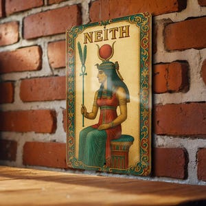 May include: Vintage metal sign featuring an illustration of the Egyptian goddess Neith. The artwork depicts Neith seated, holding a staff, with a red and gold headdress. The sign has a decorative border and the word "NEITH" at the top.