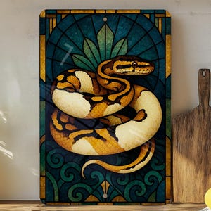 May include: A decorative metal sign featuring a coiled snake with a yellow, brown, and cream pattern. The snake is set against a teal and gold stained-glass style background. The sign is rectangular and has a hole at the top for hanging.