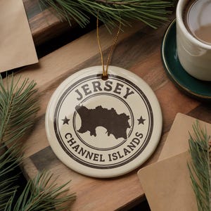 A circular ornament with the text "JERSEY CHANNEL ISLANDS" and a graphic of a map of Jersey, placed on a wooden surface with pine branches and a cup of coffee nearby.