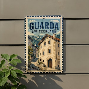 May include: A rectangular metal sign with a postage stamp edge design featuring an illustration of a village in Guarda, Switzerland. The image shows stone buildings, a cobblestone path, and mountains under a blue sky with the text GUARDA SWITZERLAND.