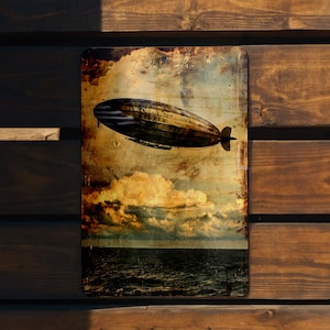May include: A vintage-style metal sign featuring a black and white image of a large airship flying over a cloudy sky and ocean. The sign has a distressed, aged look with a faded yellow background.