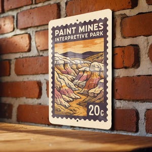 May include: A rectangular metal sign featuring a landscape illustration of Paint Mines Interpretive Park. The sign has a postage stamp design with the text "PAINT MINES INTERPRETIVE PARK" and "20c". The artwork depicts colorful rock formations.