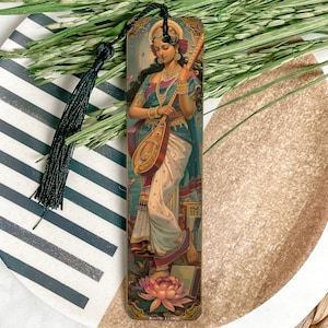 May include: A bookmark featuring a colorful illustration of a woman playing a stringed instrument. The woman is wearing a blue and white sari and a floral headpiece. The bookmark is made of wood and has a black tassel.